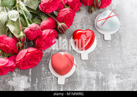 Il giorno di San Valentino o compleanno biglietto di auguri. Partita un dessert nella forma di un cuore rosso. Rose rosse e dessert su vintage tavolo in legno Foto Stock