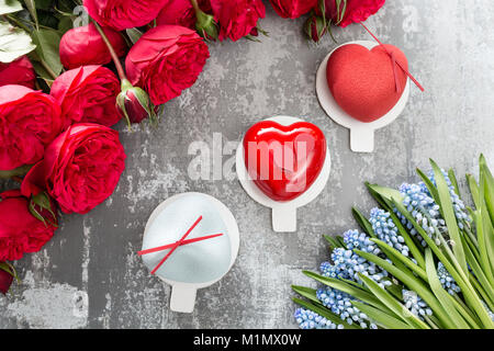 Il giorno di San Valentino o compleanno biglietto di auguri. Partita un dessert nella forma di un cuore rosso. Rose rosse e dessert su vintage tavolo in legno Foto Stock