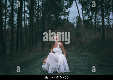 Bella donna con un ombre acconciatura, vestito di un bianco mantello tutu, in una posizione di squat, su una strada forestale, guardando in alto, in un bosco a molla. Foto Stock