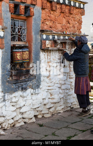 Bumthang, Bhutan. L uomo lo spostamento delle pietre a contare il numero di volte in cui egli ha filata Ruote della preghiera a Jambey Lhakhang tempio e monastero, vicino Jakar. Foto Stock