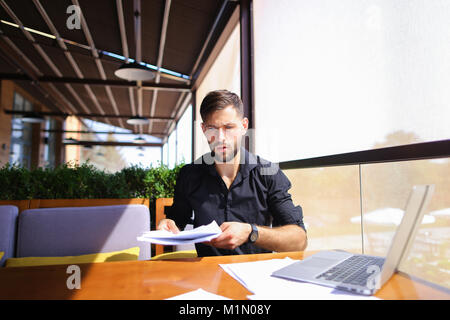 Lavoratore di ufficio ordinamento di carte sul tavolo vicino al computer portatile. Foto Stock