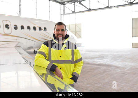 Ritratto di un meccanico aeronautico in un hangar con getti all'aeroporto - controllo del velivolo per la sicurezza e la funzione tecnica Foto Stock