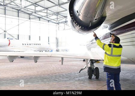 Meccanico aeronautico/ equipaggio a terra ispeziona e controlla la turbina di un jet in un hangar in aeroporto Foto Stock