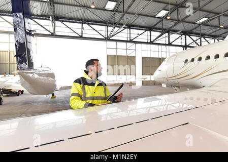 Meccanico aeronautico ispeziona e controlla la tecnologia di un getto in un hangar in aeroporto Foto Stock