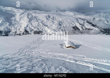 Piste da sci in polvere di nuovo fuori pista accanto ai tradizionali fienili in pietra nella valle di Belleville di 3 valli vicino a Les Menuires nelle Alpi francesi Foto Stock