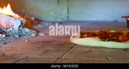 Pizza all'interno della stufa di legno durante la cottura con il fuoco e con uno sfondo di legno Foto Stock