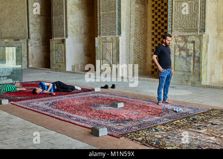 Isfahan, Iran - 24 Aprile 2017: un uomo iraniano è in piedi su un tappeto nel mezzo della moschea di Jame, due uomini stanno dormendo dietro di lui. Foto Stock