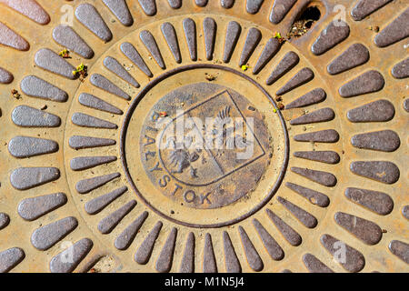 Vecchio ghisa fognatura boccaporto coprire con lo stemma della città Bialystok, Polonia. Tombino di ferro sulla strada della grande città Foto Stock