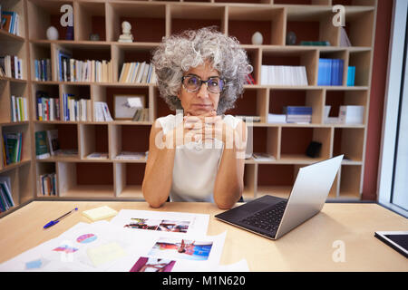 Senior imprenditrice utilizzando computer portatile in ufficio guarda alla fotocamera Foto Stock