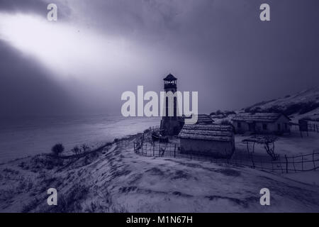 Il vecchio faro di legno nella notte a bordo del porto di congelati con cielo nuvoloso. Blu luce atmosferica Foto Stock