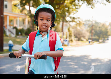 Giovane ragazzo Scooter equitazione lungo la strada alla scuola Foto Stock