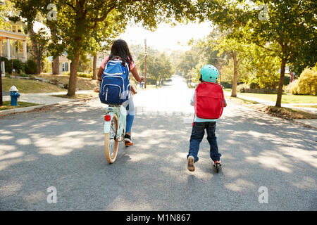 Sorella con fratello Equitazione Scooter e Bici a scuola Foto Stock