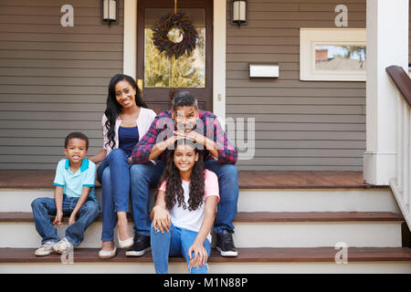 Famiglia con bambini seduti sulla scalinata che conduce al portico di casa Foto Stock