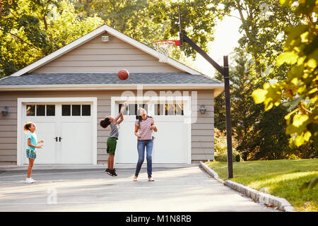 Madre e bambini giocare a basket sulla strada di casa Foto Stock