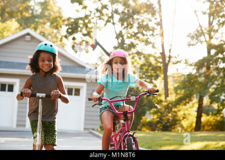 Sorella con fratello Equitazione Scooter e Bici sul vialetto a casa Foto Stock