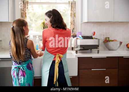 Mamma e figlia lavando le mani al lavello da cucina, vista posteriore Foto Stock