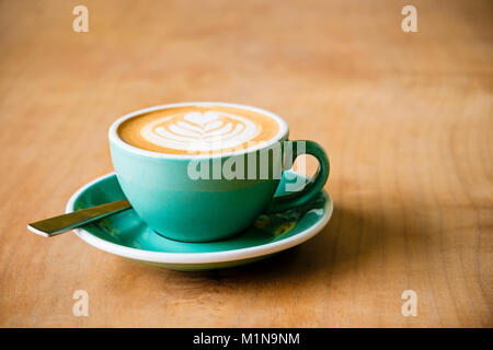 Una tazza di caffè con latte art di una foglia in schiuma con un cucchiaio su una tavola di legno Foto Stock