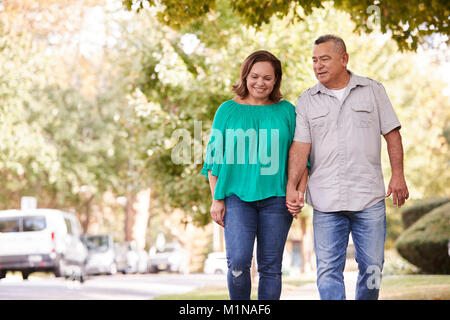 Coppia senior a piedi lungo la strada suburbana tenendo le mani Foto Stock