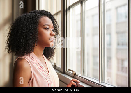 Giovane nero imprenditrice guardando fuori della finestra Foto Stock