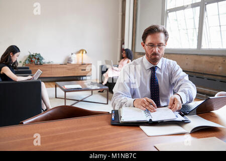 Imprenditore lavorare alla scrivania, colleghe in background Foto Stock