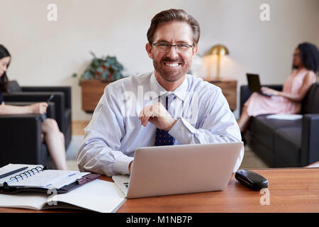 Uomo d affari con computer portatile alla reception sorride alla telecamera Foto Stock