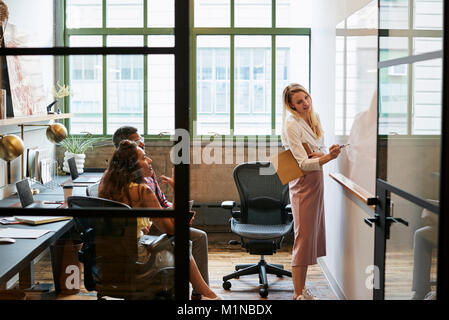 Donna alla lavagna nella riunione del team, visto attraverso la porta aperta Foto Stock