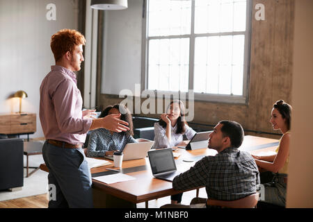 Giovane uomo in piedi per affrontare i colleghi ad una riunione di lavoro Foto Stock