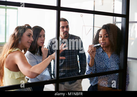 Giovani colleghi in una riunione visualizzazione su una parete di vetro Foto Stock