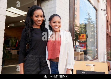 Due giovani donne a sorridere alla telecamera al di fuori del loro negozio di abbigliamento Foto Stock