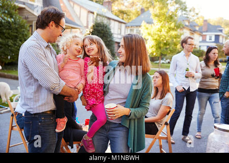 I genitori tenendo i loro bambini mentre mangiano in un block party Foto Stock