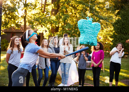 Amici guardare la ragazza adolescente di colpire una piñata per il suo compleanno Foto Stock