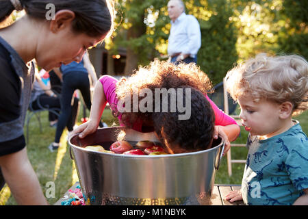 Amici guardare la pre-teen ragazza bobbing apple al partito del cortile Foto Stock