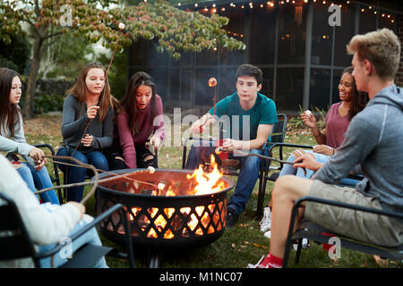 Amici di adolescenti sedersi attorno a una buca per il fuoco la tostatura marshmallow Foto Stock