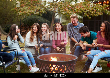 Amici di adolescenti sedersi attorno a una buca per il fuoco la tostatura marshmallow Foto Stock