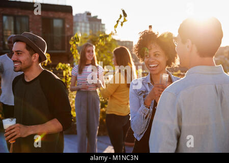 Happy amici ad una festa sul tetto retroilluminati da luce solare Foto Stock