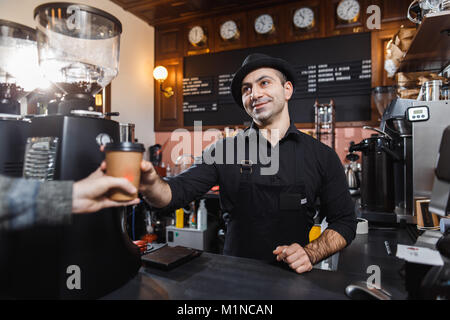 Positivo maschio barista vendita del caffè per un consumatore in una caffetteria. Foto Stock