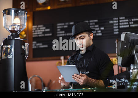 Ritratto del barista azienda digitale compressa al contatore nel coffee shop. Foto Stock