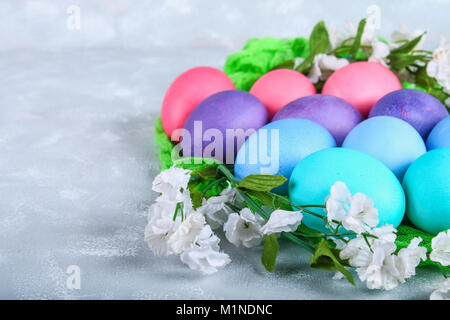 Colorate le uova di pasqua con fiori di colore bianco su un cemento grigio sfondo Foto Stock
