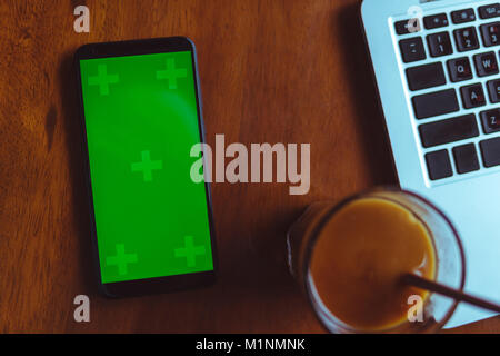 Scrivania da ufficio Tavolo con laptop, smartphone con schermo verde e caffè Foto Stock