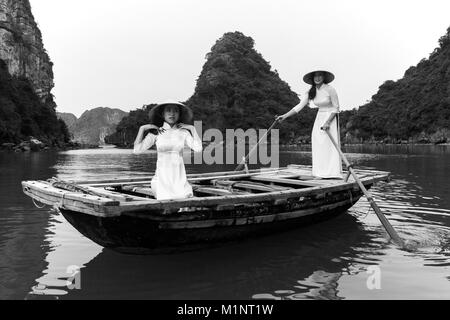 Le giovani donne che posano su un canotto tradizionale nella baia di Halong, Vietnam. Le isolette di calcare e di formazioni rocciose sono diventati un'UNESCO area protetta. Foto Stock