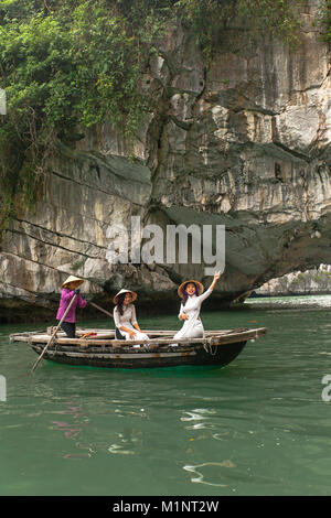 Giovani donne in posa su una barca a remi al di fuori di una caverna nella baia di Halong, Vietnam. Le isolette di calcare e di formazioni rocciose sono diventati un'UNESCO area protetta. Foto Stock