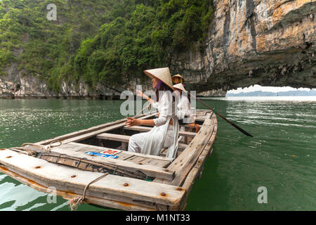 Giovani donne in posa su una barca a remi al di fuori di una caverna nella baia di Halong, Vietnam. Le isolette di calcare e di formazioni rocciose sono diventati un'UNESCO area protetta. Foto Stock