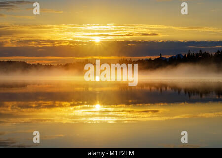 Con sunrise early morning mist over Kirchsee con Monastero Reutberg,Sachsenkam,Alta Baviera, Baviera, Germania Foto Stock