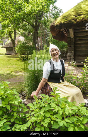 Donna in abito tradizionale al di fuori del xvii secolo cascina, Etnografico lettone Open Air Museum, Riga, Lettonia, Europa Foto Stock