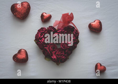 Forma di cuore costituita da piccole rose circondata con i cuori più piccoli sulla parte superiore di un letto bianco foglio. Foto Stock