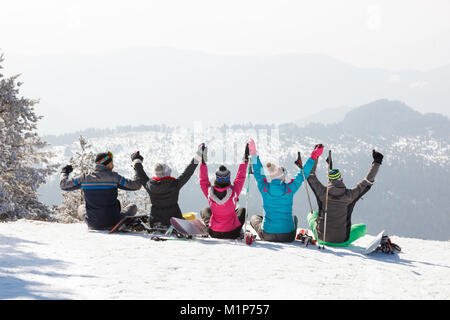Gruppo di sciatori guardando lo splendido paesaggio mentre è seduto sulla neve in montagna, vista posteriore Foto Stock