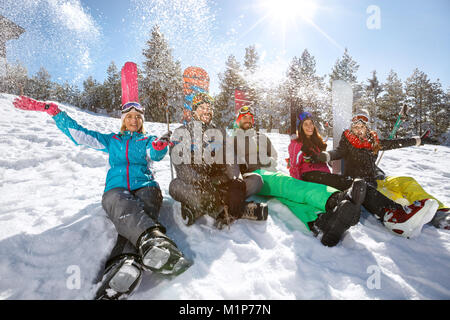 Felice gruppo di giovani sciatori seduti sulla neve e godendo Foto Stock