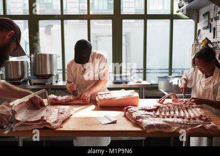 Tre macellai di preparazione della carne di maiale in una macelleria Foto Stock