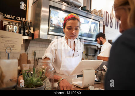 Giovane donna che serve un cliente in una macelleria Foto Stock