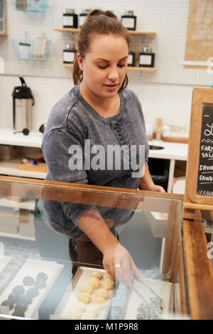 Giovane donna disponendo il contatore di pasticceria in una pasticceria Foto Stock
